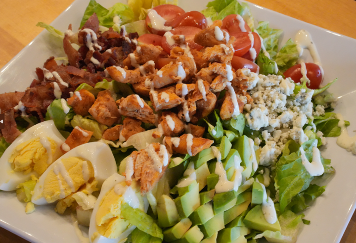 Square plate topped with chicken, hard boiled egg slices, bleu cheese crumbles, avocado and sliced cherry tomatoes