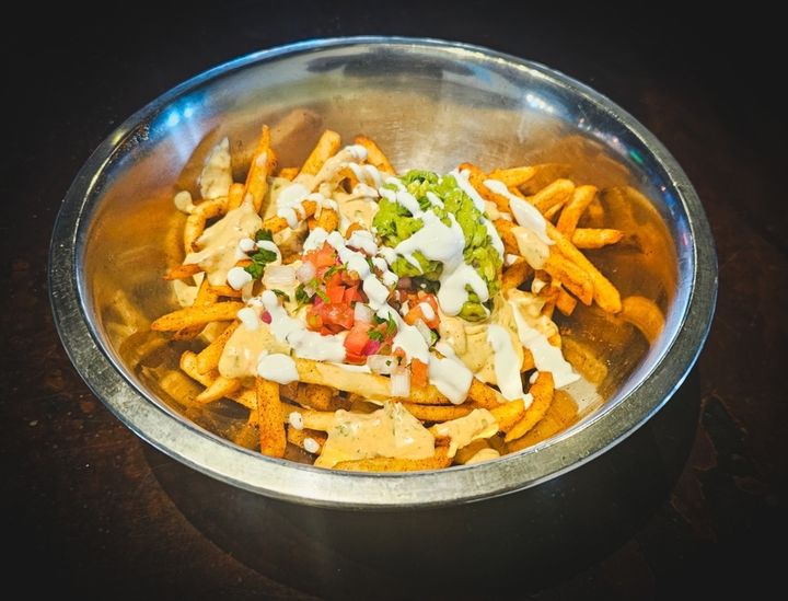 Bowl of fries topped with melted cheese, sour cream and guacamole
