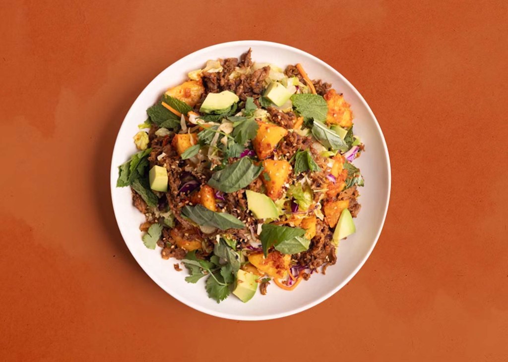 Plate of salad featuring bright green cilantro and avocado, mixed with beef and pineapple kimchee